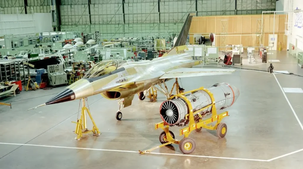 Il propulsore turbofan Pratt & Whitney F100 sul carrello di montaggio davanti al primo prototipo dell'YF-16 (s/n 72-1567). La foto, scattata negli stabilimenti General Dynamics di Fort Worth alla fine del 1973, mostra la cellula sollevata sui martinetti idraulici prima dell'integrazione del motore. (Foto: U.S. Air Force / General Dynamics)