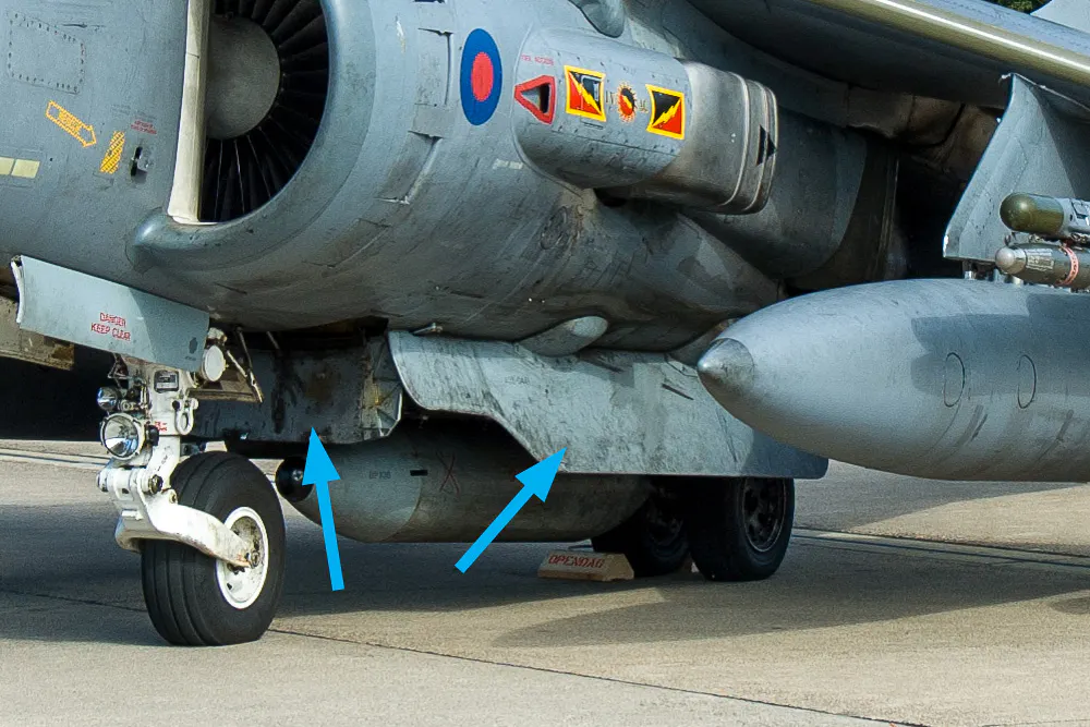 Nella foto, le alette indicate dalle frecce azzurre sono i dispositivi di miglioramento della portanza (LIDS), specifici dell'Harrier II. Questi elementi strutturali hanno lo scopo di intrappolare i flussi di scarico dei motori che rimbalzano sul terreno durante il decollo e l'atterraggio verticale: catturando quest'aria ad alta energia sotto la pancia della fusoliera, i LIDS creano un cuscino ad alta pressione che fornisce una spinta verticale extra e, al contempo, riduce il fenomeno del risucchio negativo (suckdown) e il ricircolo dei gas caldi verso le prese d'aria.