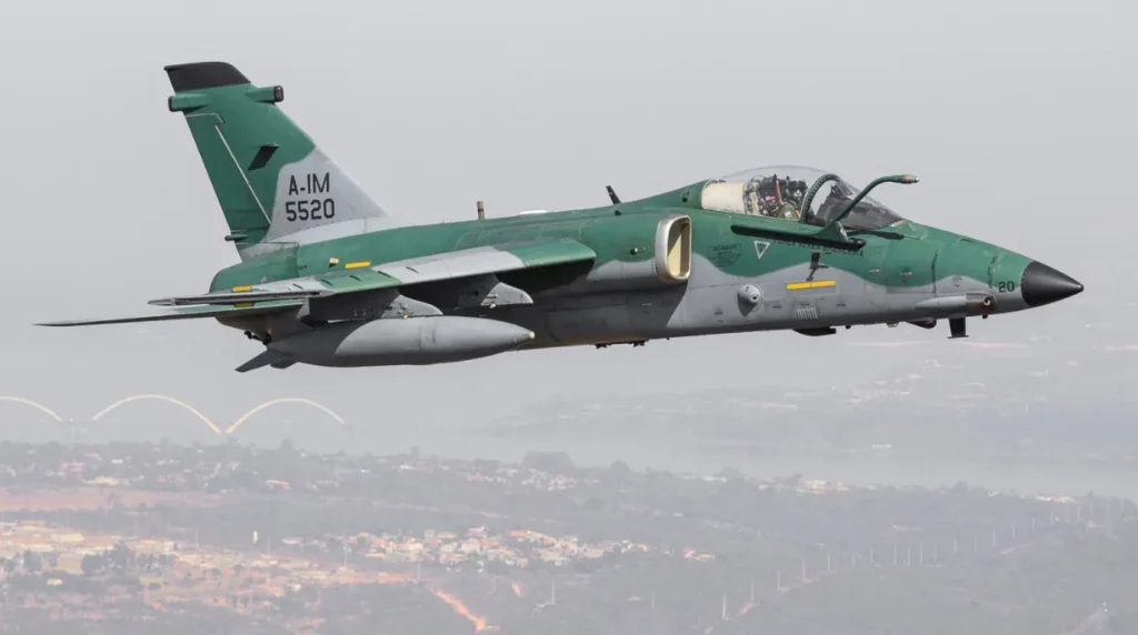 Un caccia d'attacco Embraer A-1M AMX modernizzato (s/n 5520) della Força Aérea Brasileira in volo a bassa quota con mimetica verde e grigia.