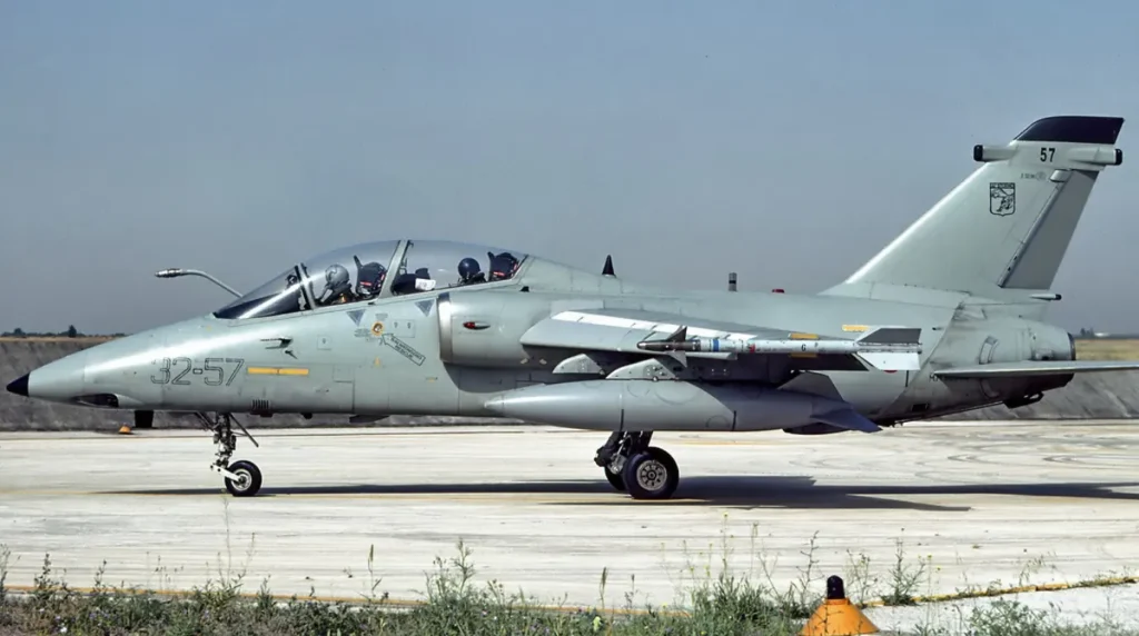 Un caccia bombardiere biposto AMX-T (codice 32-57) del 32° Stormo dell'Aeronautica Militare Italiana a terra sulla pista, equipaggiato con serbatoi ausiliari e missile AIM-9 Sidewinder inerte alle estremità alari.