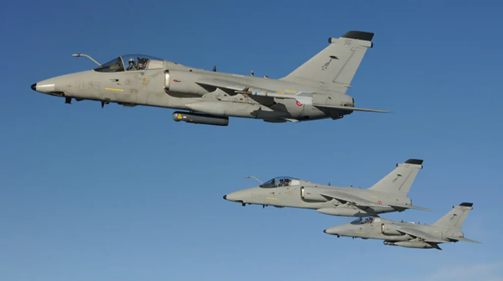 Formazione in volo di tre caccia bombardieri leggeri AMX Ghibli ACOL del 51° Stormo dell'Aeronautica Militare Italiana con livrea grigia a bassa visibilità su sfondo cielo azzurro.