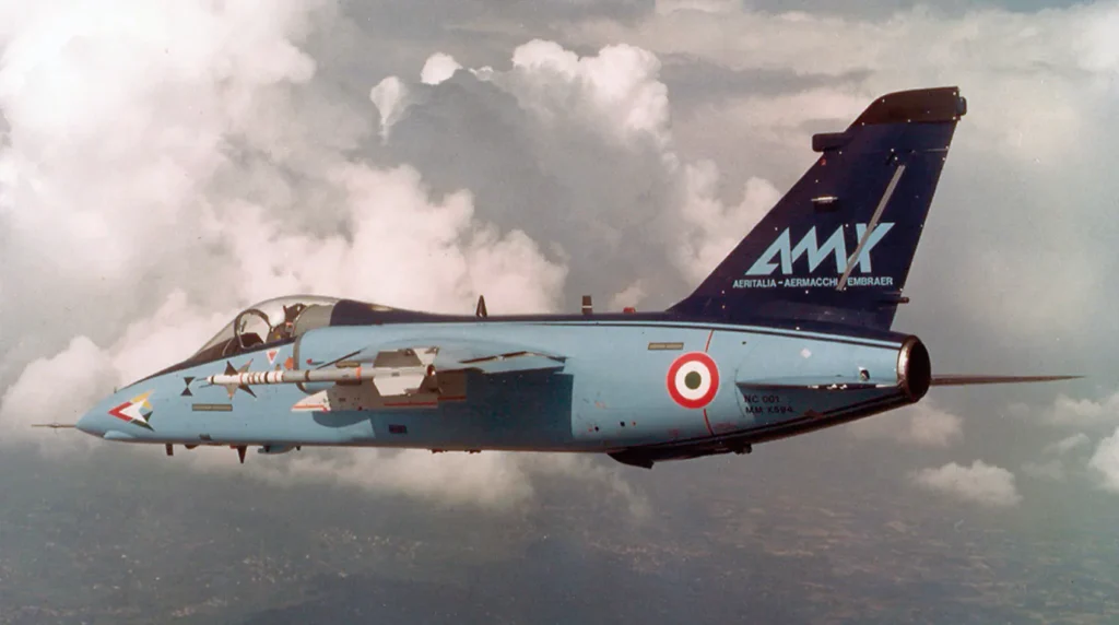Il primo prototipo del caccia italo-brasiliano AMX (matricola MM X594) in volo, con i loghi storici delle aziende costruttrici Aeritalia, Aermacchi ed Embraer sulla deriva azzurra.