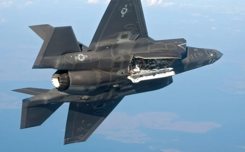 Caccia stealth F-35 Lightning II in volo virato con il portellone della stiva interna aperto che mostra un missile aria-aria AIM-120 AMRAAM pronto al lancio.