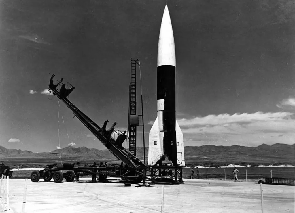 Il Meillerwagen e il V-2 a White Sands Proving Ground, 1946. Un'immagine rara e storica che cattura il processo di preparazione al lancio del missile V-2 (A-4) dopo la sua cattura dall'esercito americano. Il Meillerwagen, un veicolo specializzato per il trasporto e il sollevamento del missile, lo posiziona sulla sua piattaforma di lancio per una serie di test che hanno gettato le basi per l'esplorazione spaziale.