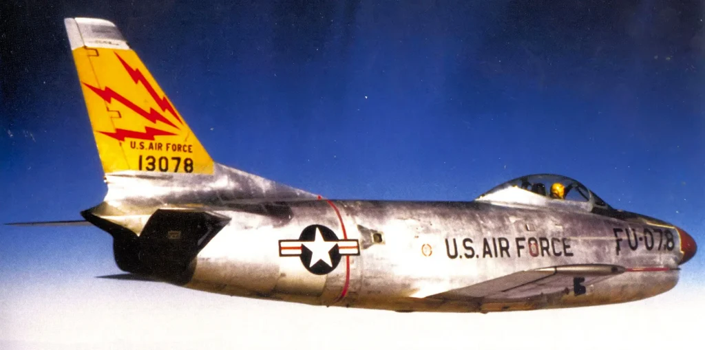 Un raro scatto a colori dell’F-86D "Sabre Dog" appartenente al 465th FIS. Il riflesso radente del sole sulla fusoliera esalta la finitura metal-less (metallo naturale) del velivolo, mettendo splendidamente in risalto le leghe metalliche e le pannellature di cui era interamente vestito il "Dog".