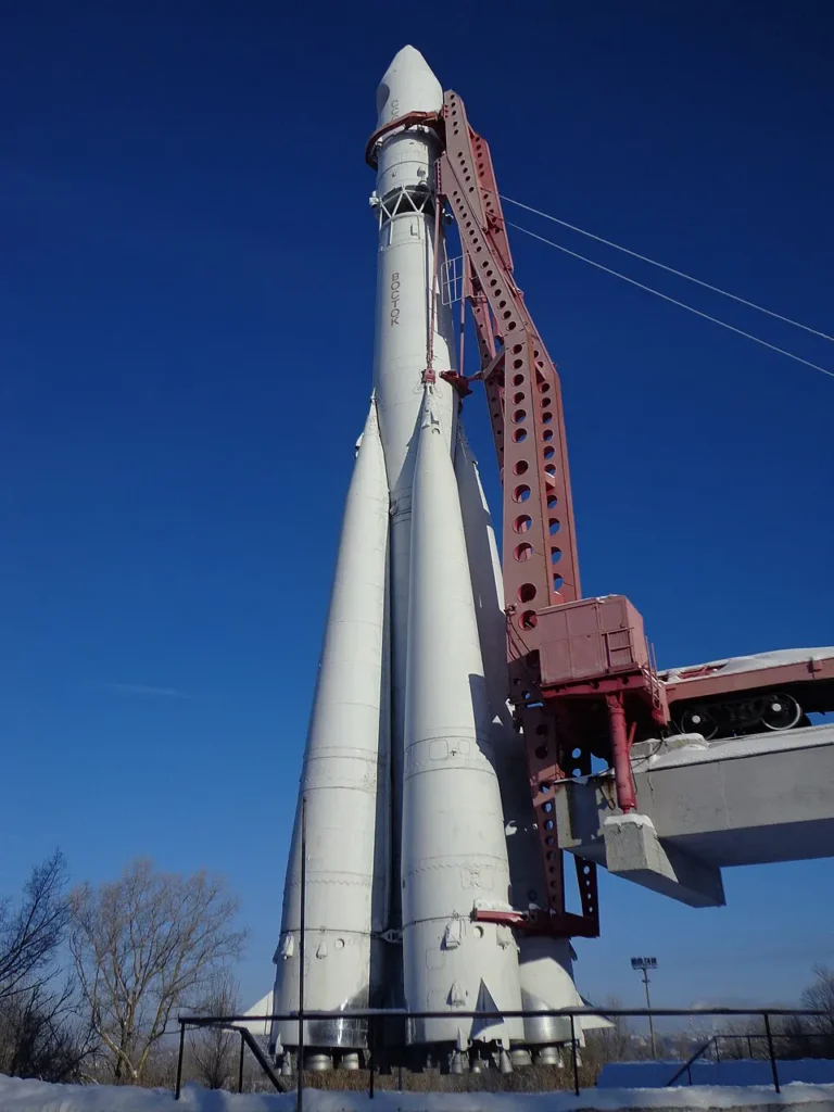 L'evoluzione finale dell'R-7: Il monumento al razzo vettore Vostok a Kaluga, in Russia. Questa imponente struttura mostra la configurazione definitiva derivata dal missile intercontinentale R-7 progettato da Sergej Korolëv. Si noti l'architettura unica a "mazzo", con i quattro grandi booster laterali avvolti attorno al corpo centrale, e la colossale struttura di servizio metallica arancione utilizzata per issare il razzo in verticale sulla rampa. È il vettore autarchico che l'Unione Sovietica utilizzò per lanciare lo Sputnik e, nel 1961, per portare Jurij Gagarin nello spazio.