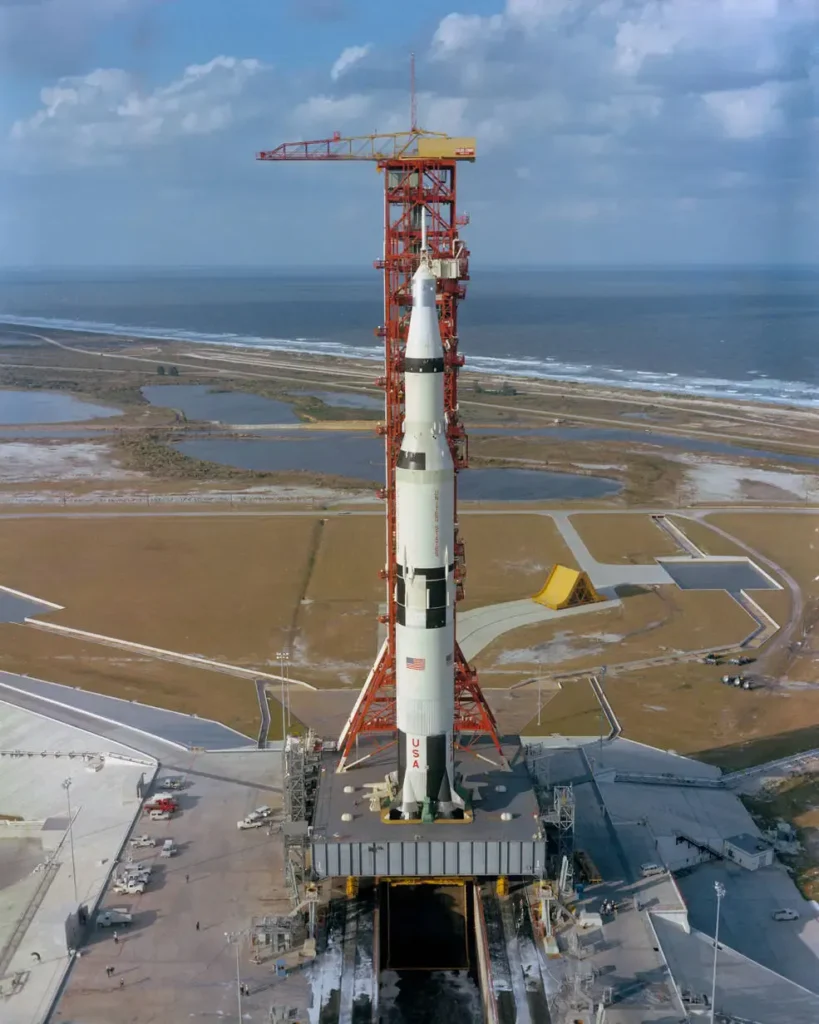 Il gigante di Cape Canaveral pronto alla sfida: Il colossale razzo vettore Saturn V posizionato sulla rampa di lancio del Kennedy Space Center, a ridosso dell'Oceano Atlantico. Sviluppato dalla NASA sotto la direzione di Wernher von Braun e del Marshall Space Flight Center, questo titano a propellente liquido di 111 metri rappresenta la massima evoluzione ingegneristica della corsa allo spazio. L'immagine mostra il vettore agganciato alla torre di lancio mobile rossa, l'imponente struttura di servizio flessibile che riforniva i tre stadi di propellente criogenico prima del decollo e che ha permesso alle missioni Apollo di raggiungere la Luna. (Foto: NASA)